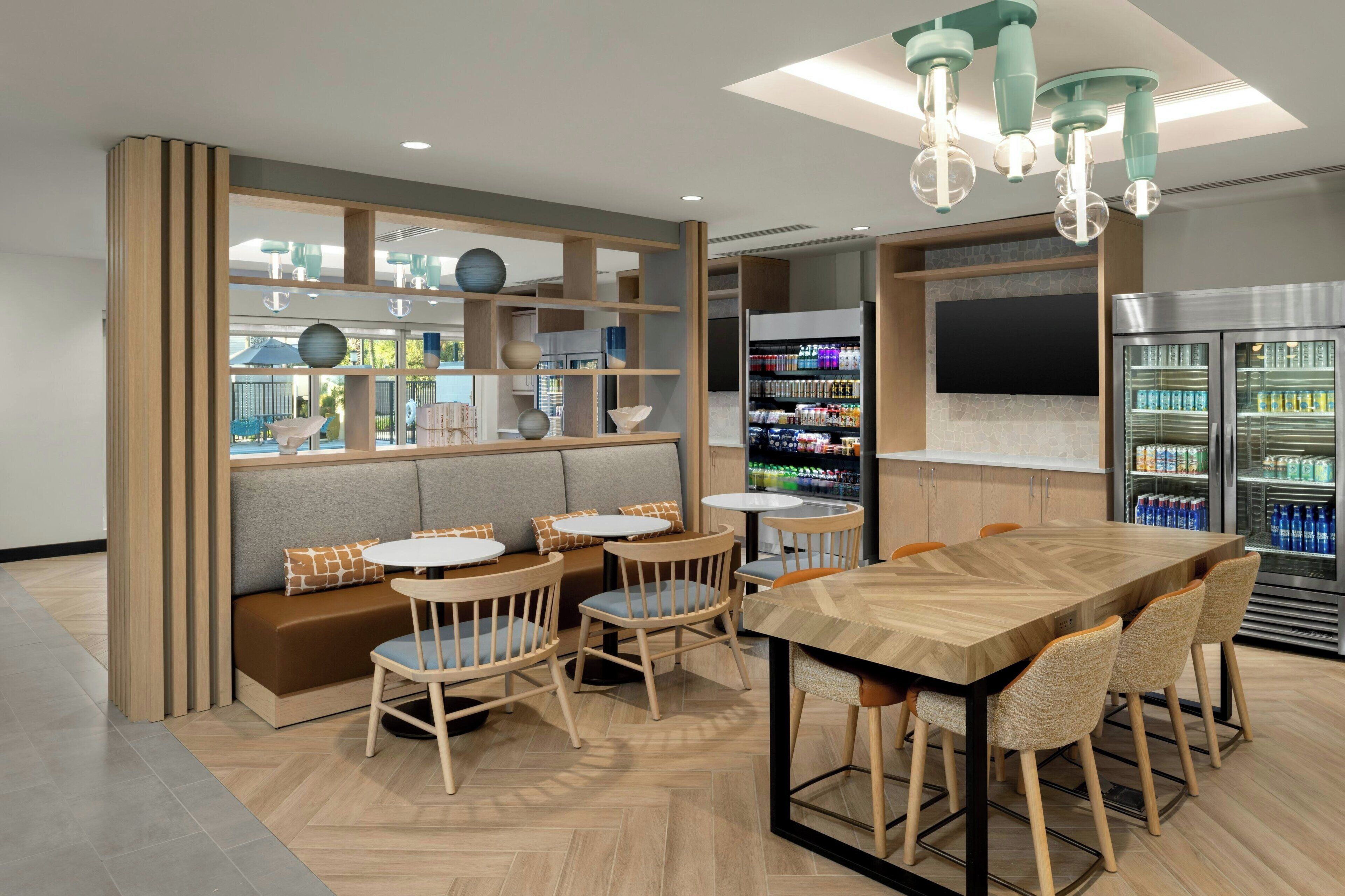 A modern cafe with a wooden dining table, cushioned seating, and a variety of beverages in the background.