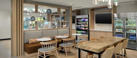 A modern cafe with a wooden dining table, cushioned seating, and a variety of beverages in the background.