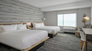 Ein Hotelzimmer mit zwei Betten, einem Schreibtisch, einem Stuhl, einer Lampe und einem großen Fenster.