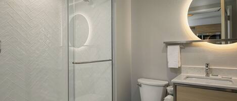 Un baño moderno con cabina de ducha de vidrio, inodoro y tocador con espejo.