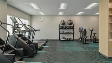 A gym with treadmills, elliptical machines, and a wall-mounted equipment rack.
