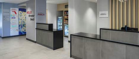 Un área de recepción moderna de hotel con un mostrador, un refrigerador lleno de bebidas y una pared con un letrero que dice 'Hello Pinch'.