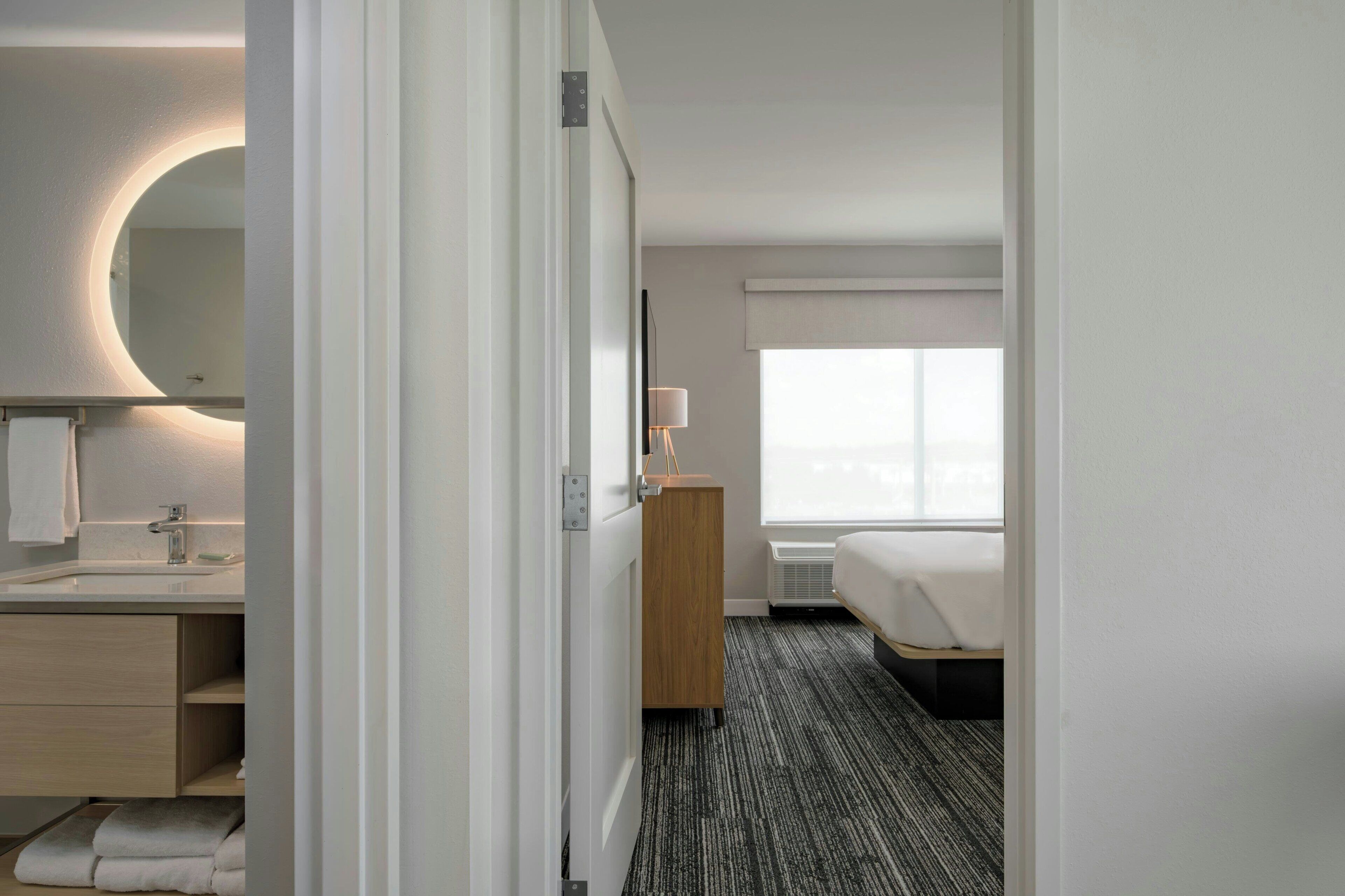 Une chambre d’hôtel avec une salle de bain, un lit, une table de chevet, une lampe et une fenêtre.