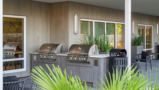 Eine Terrasse im Freien mit zwei Grillanlagen, einer Sitzecke mit Stühlen und Blumentöpfen.