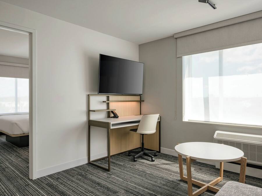 A modern hotel room with a desk, chair, TV, and a small table.