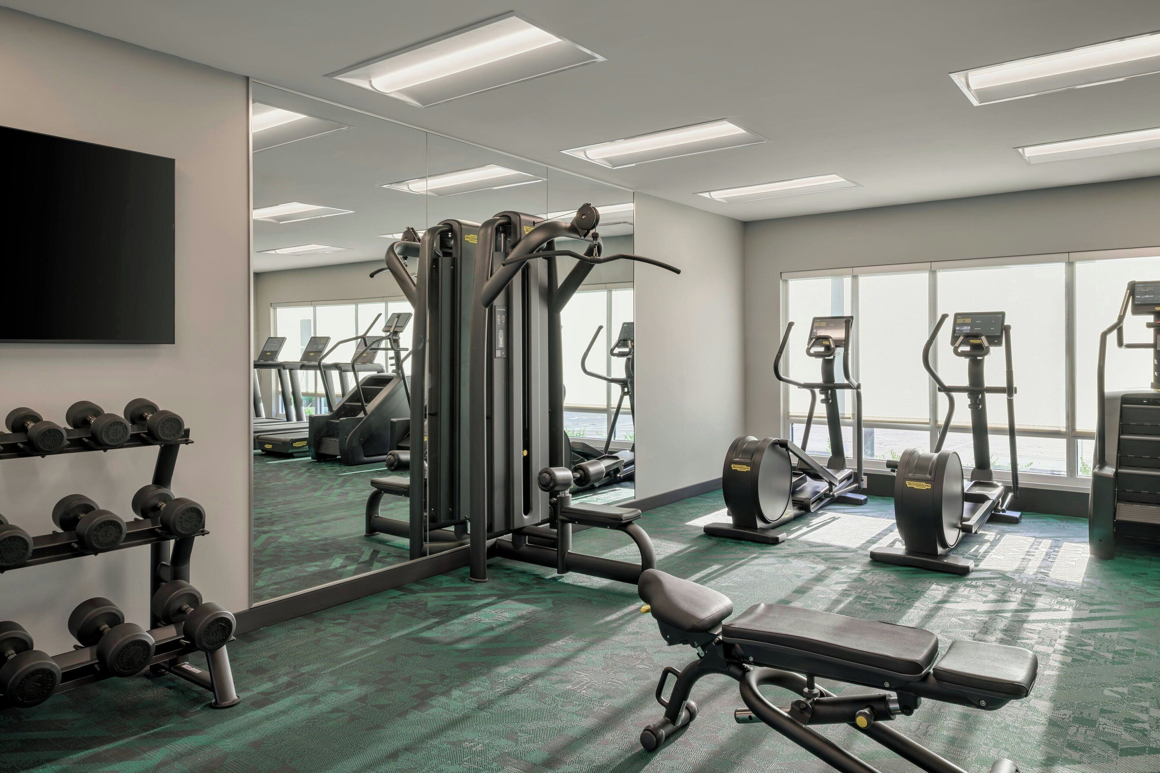 Une salle de sport équipée de matériel d’exercice, d’un banc et d’un téléviseur fixé au mur.