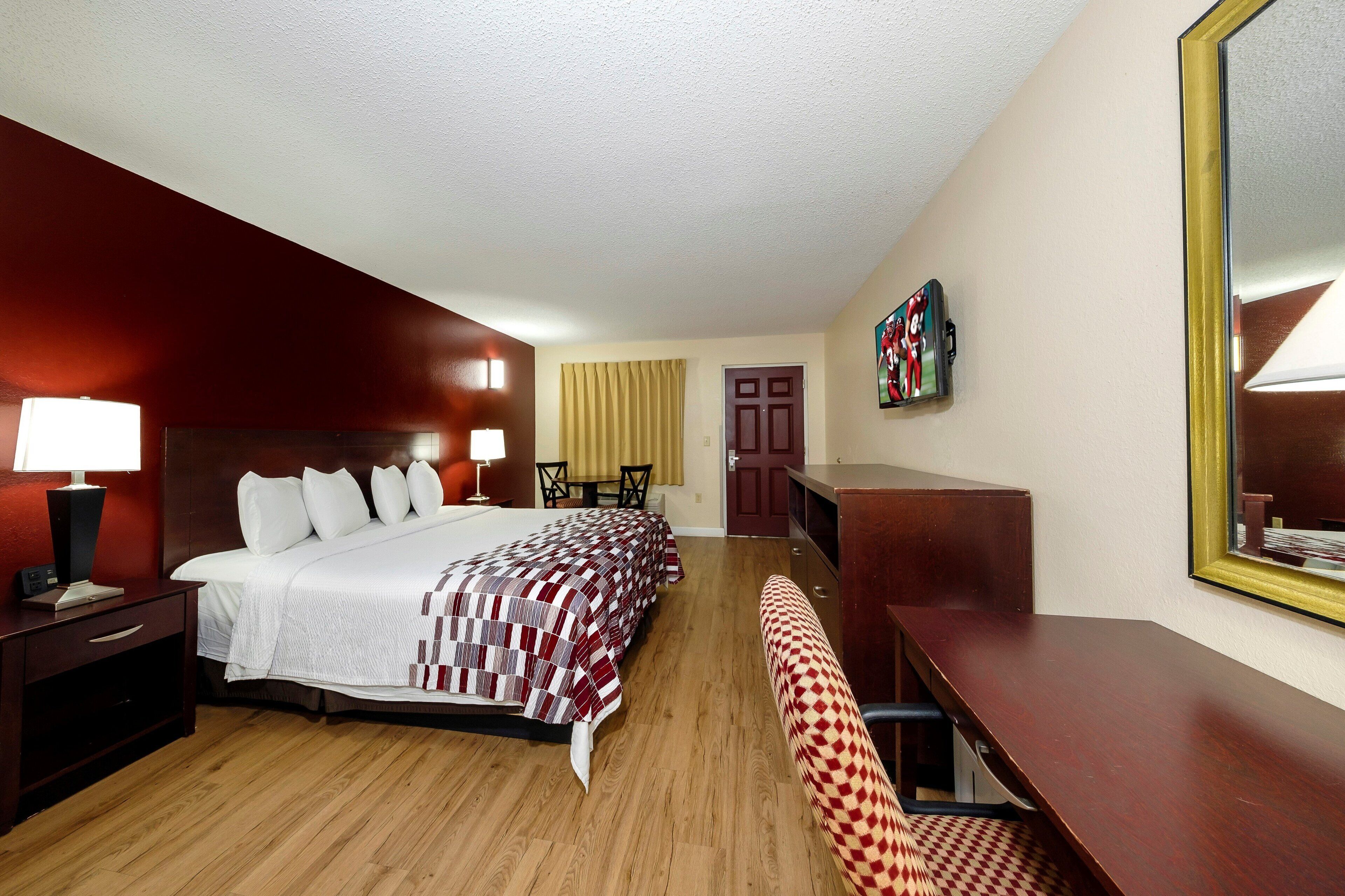 A hotel room with a bed, bedside tables, a desk, a chair, a television, and a door.