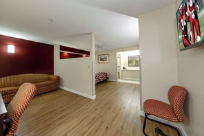 A living room with a sofa, a chair, and a television mounted on the wall. - Red Roof Inn Ellenton – Bradenton NE (Ellenton)