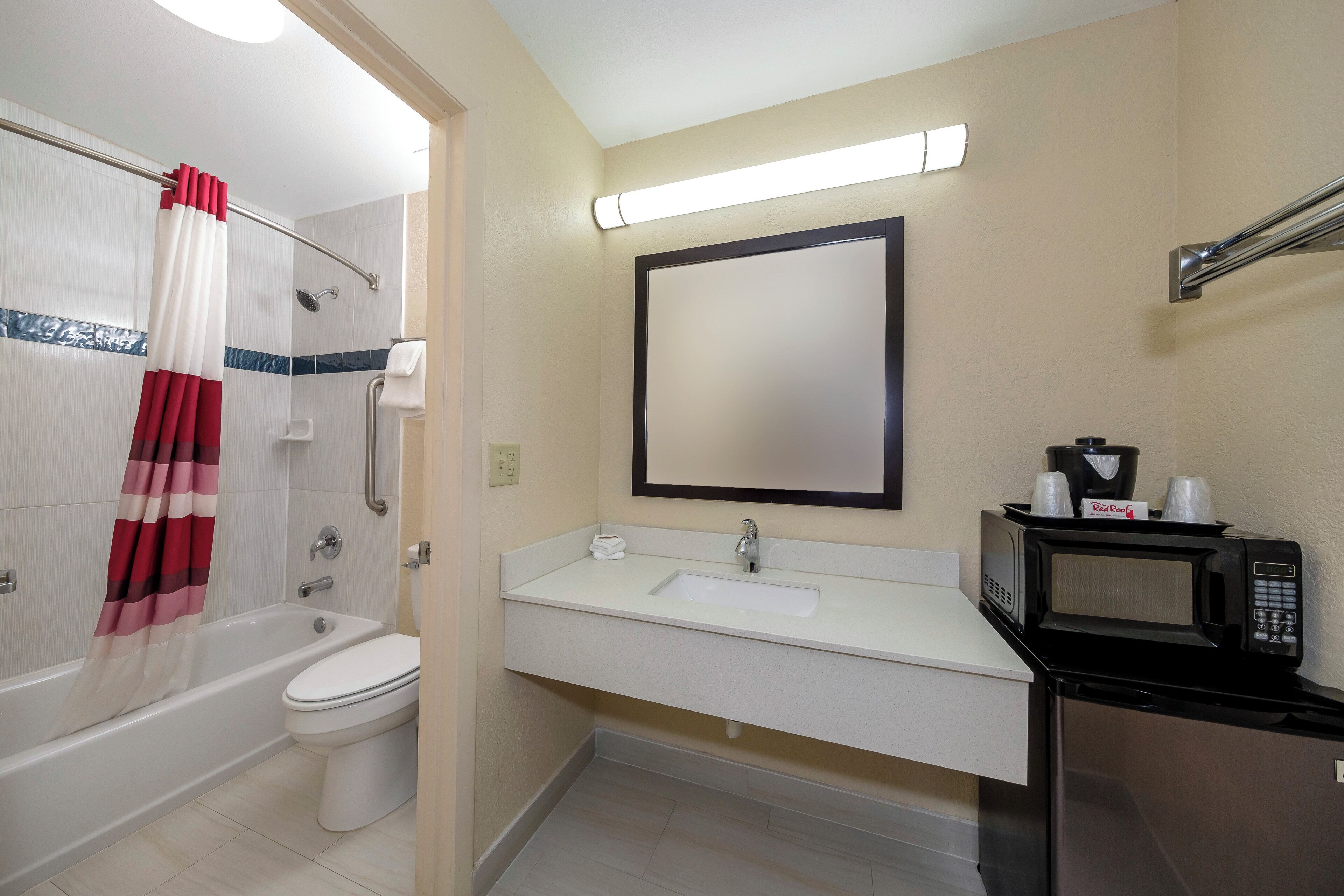 Un baño con bañera, inodoro, lavabo y un microondas.
