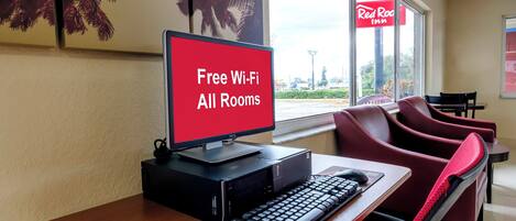Un bureau d’ordinateur avec un écran affichant la mention « Wi-Fi gratuit dans toutes les chambres » dans une chambre d’hôtel.