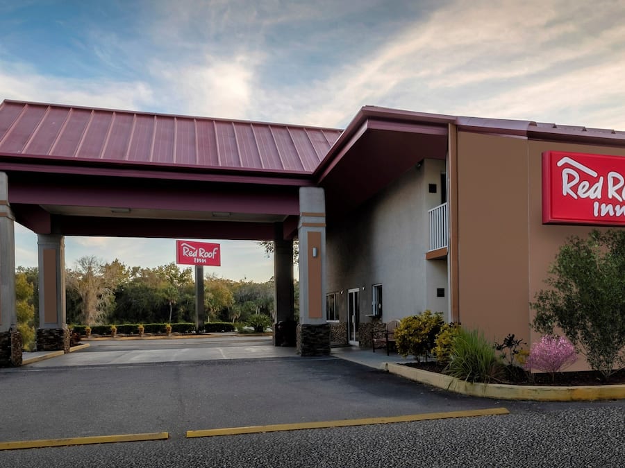 Et Red Roof Inn hotel med overdækket indgang, parkeringsplads og anlagt område med buske og træer.