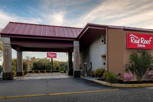 Un hôtel Red Roof Inn doté d’une entrée abritée, d’un parking et d’un espace paysager agrémenté d’arbustes et d’arbres.
