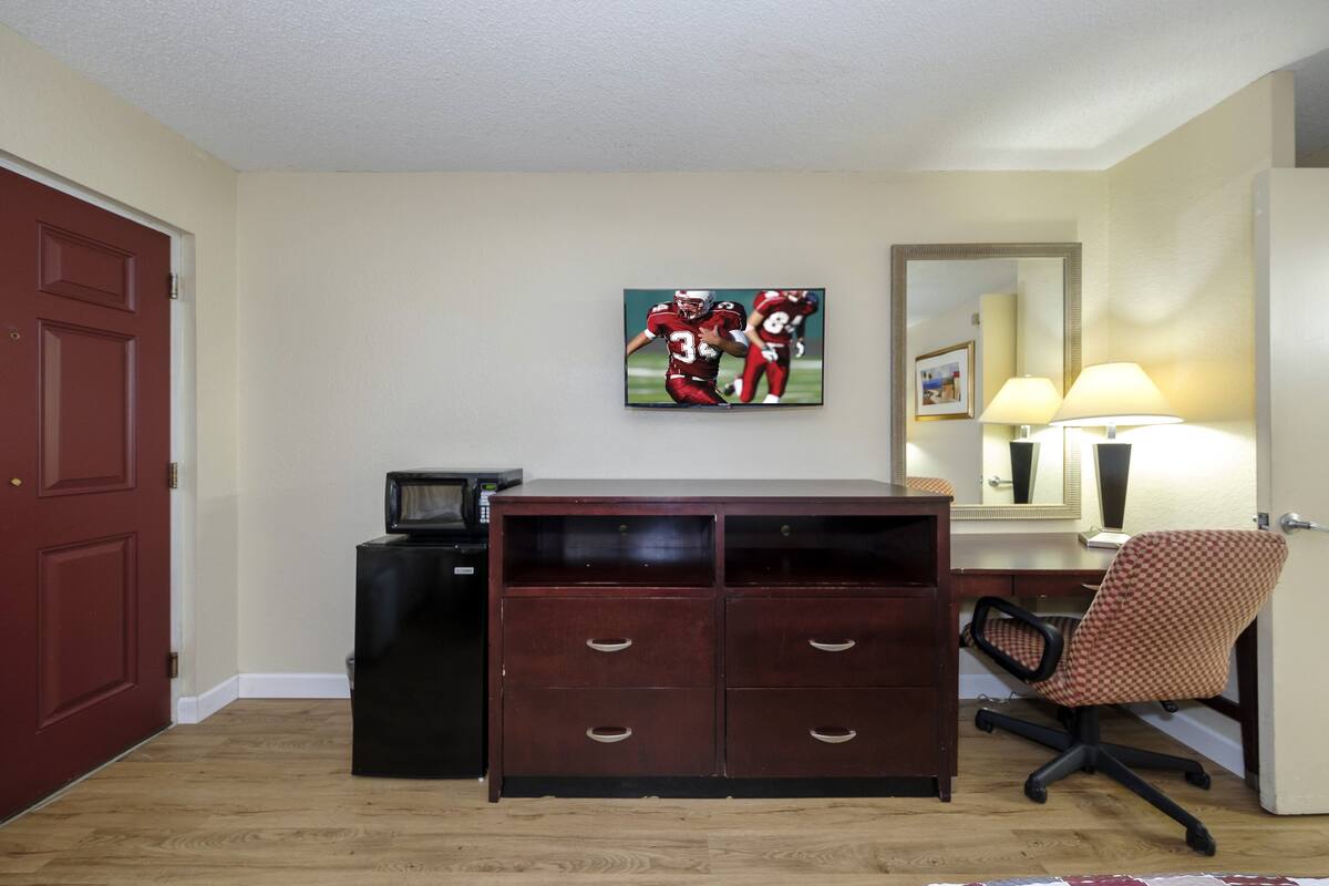 A room with a wooden desk, a chair, a television, and a painting on the wall.