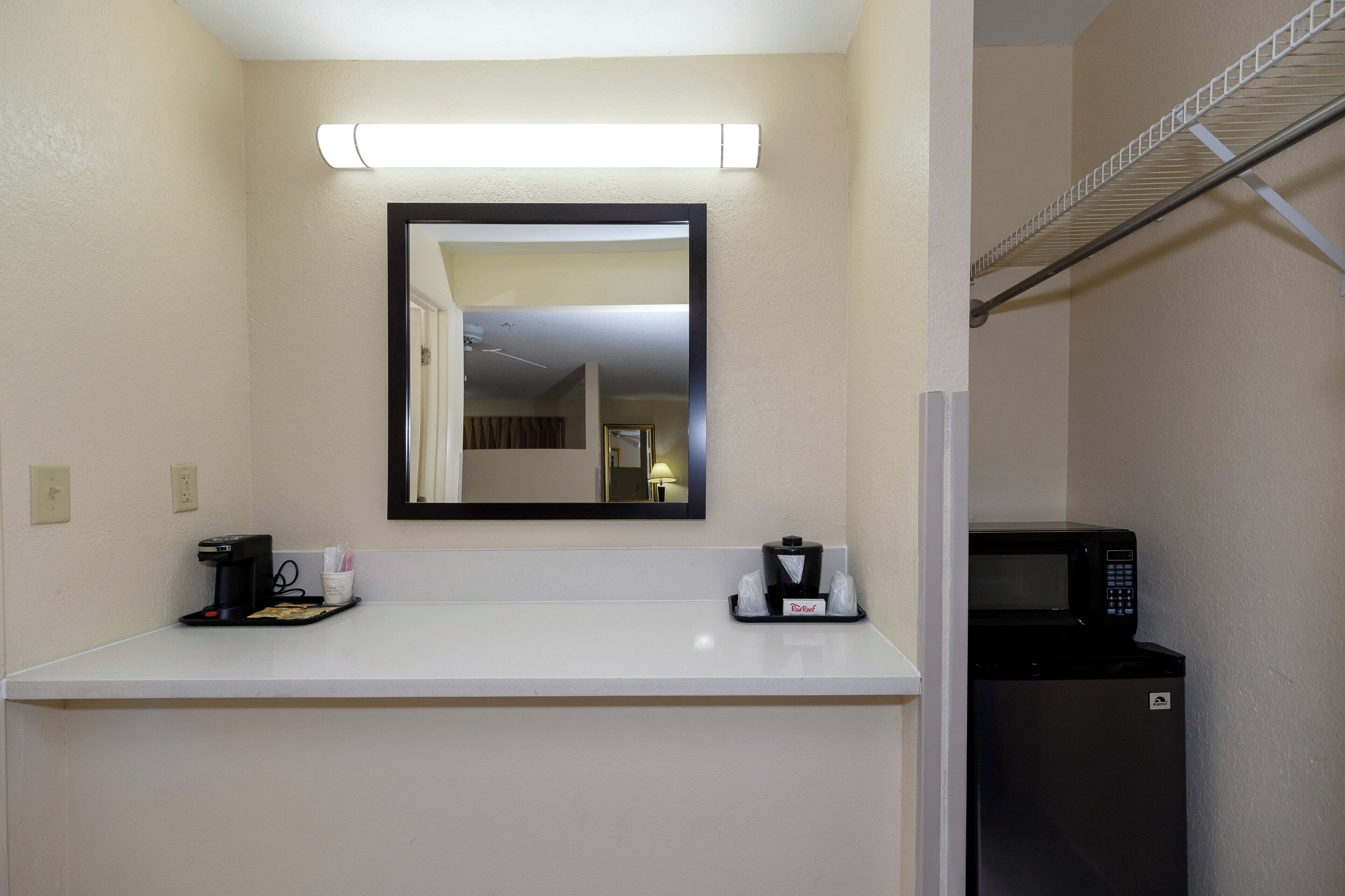Habitación de hotel con una encimera blanca, cafetera, microondas y un espejo sobre la encimera.