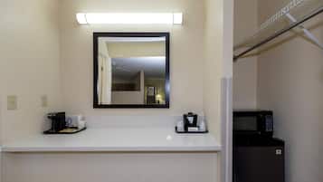 Habitación de hotel con una encimera blanca, cafetera, microondas y un espejo sobre la encimera.
