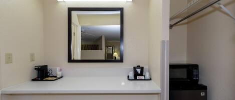 A hotel room with a white countertop, a coffee maker, a microwave, and a mirror above the counter.
