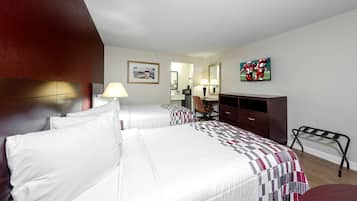 Habitación de hotel con dos camas, un escritorio, una silla, un televisor y obras de arte en las paredes.