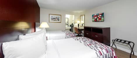 A hotel room with two beds, a desk, a chair, a television, and artwork on the walls.
