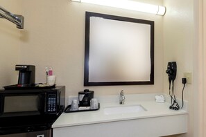 Une salle de bain d’hôtel équipée d’un lavabo, d’un miroir, d’une machine à café et d’un sèche-cheveux.