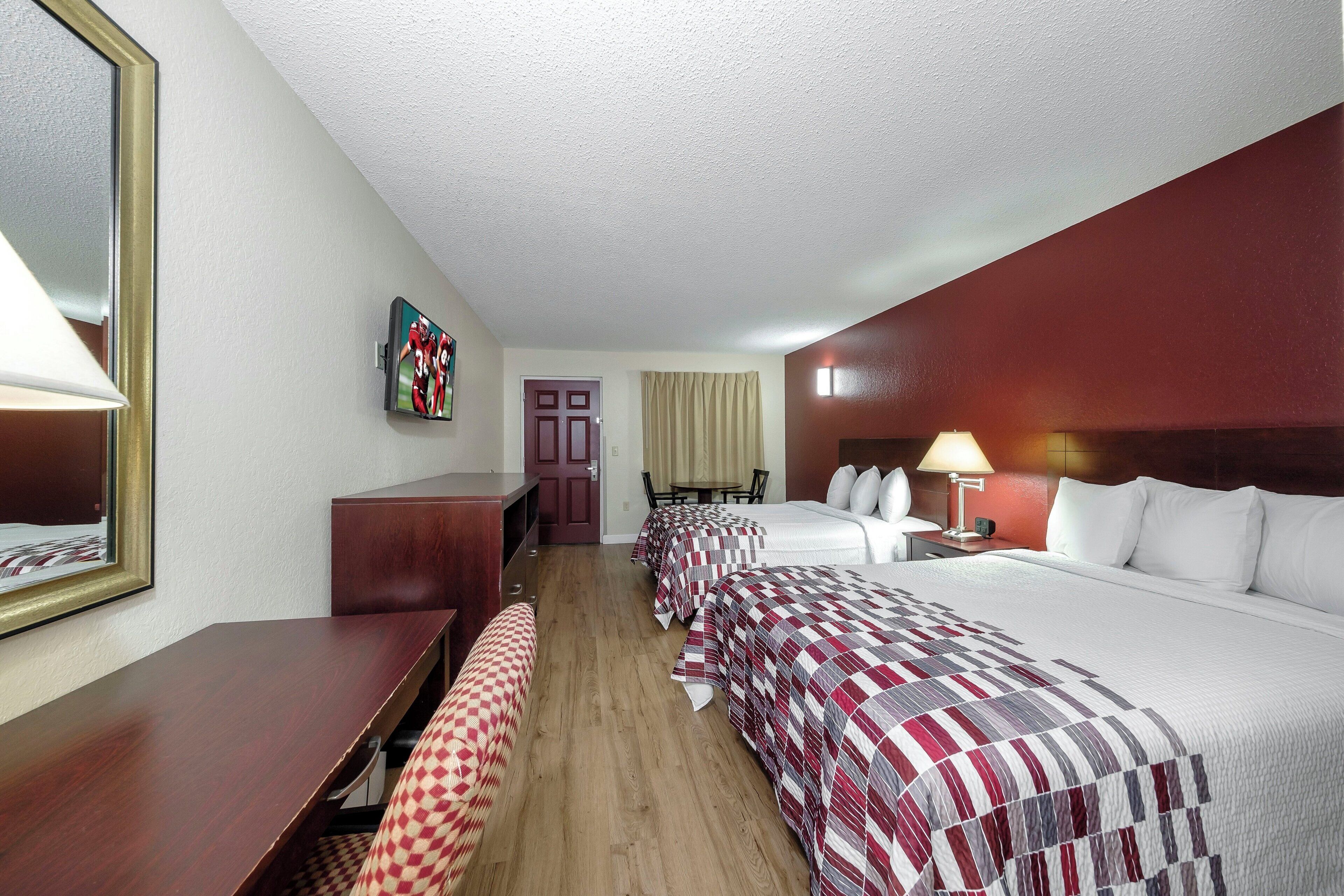 Una habitación de hotel con cama, escritorio, silla, televisor y puerta.