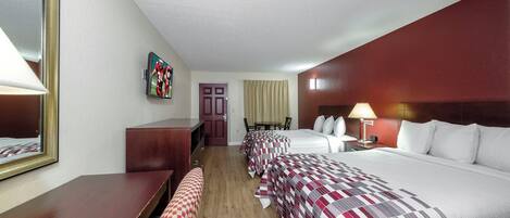 Quarto de hotel com cama, escrivaninha, cadeira, televisão e porta.