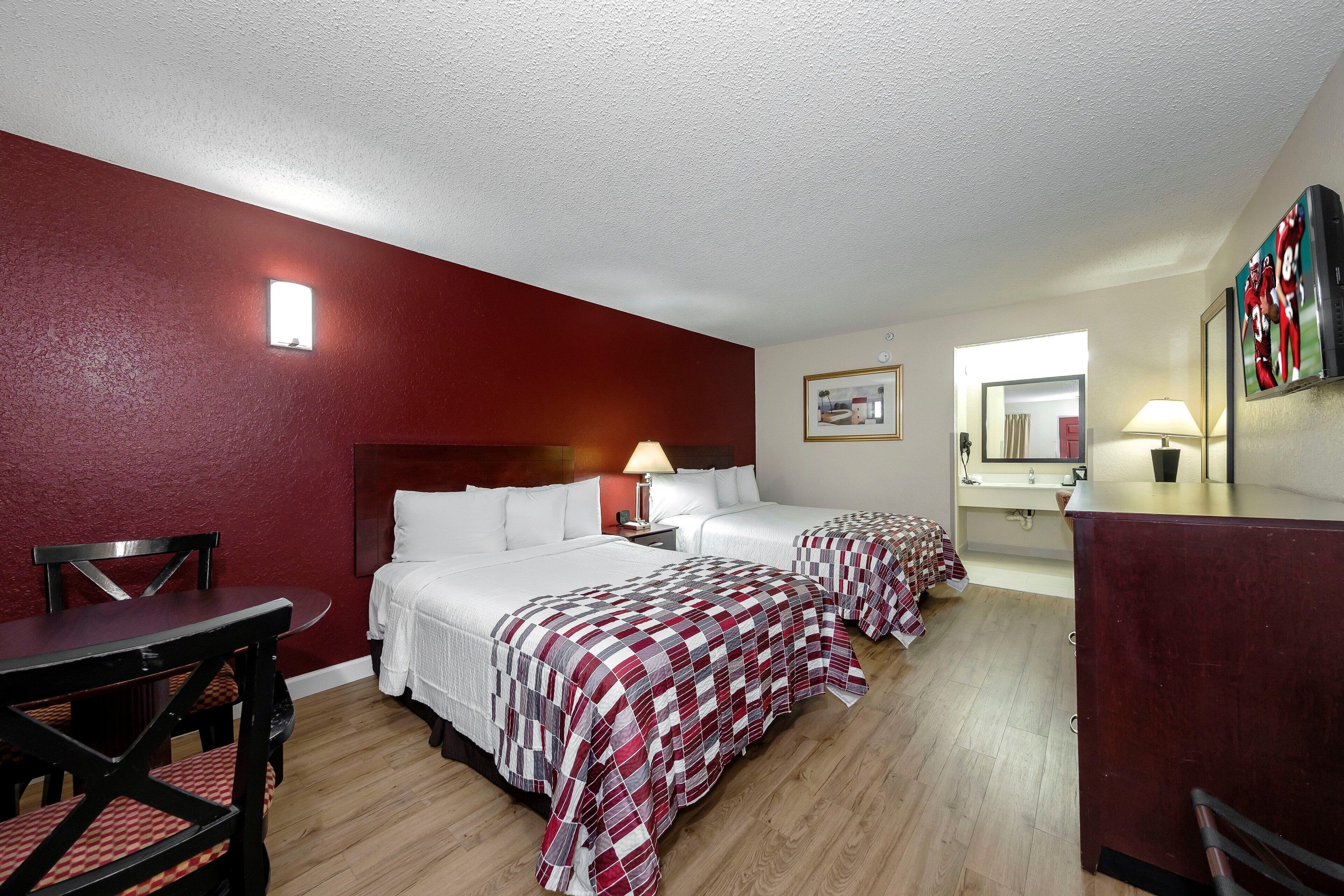 A hotel room with two beds, a desk, a chair, and a TV.
