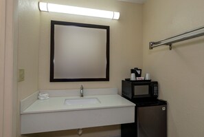 Une salle de bain avec un lavabo blanc, un miroir, un porte-serviettes, un four à micro-ondes et une poubelle.