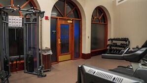 A gym with exercise equipment, a door with a blue light, and an exit sign.