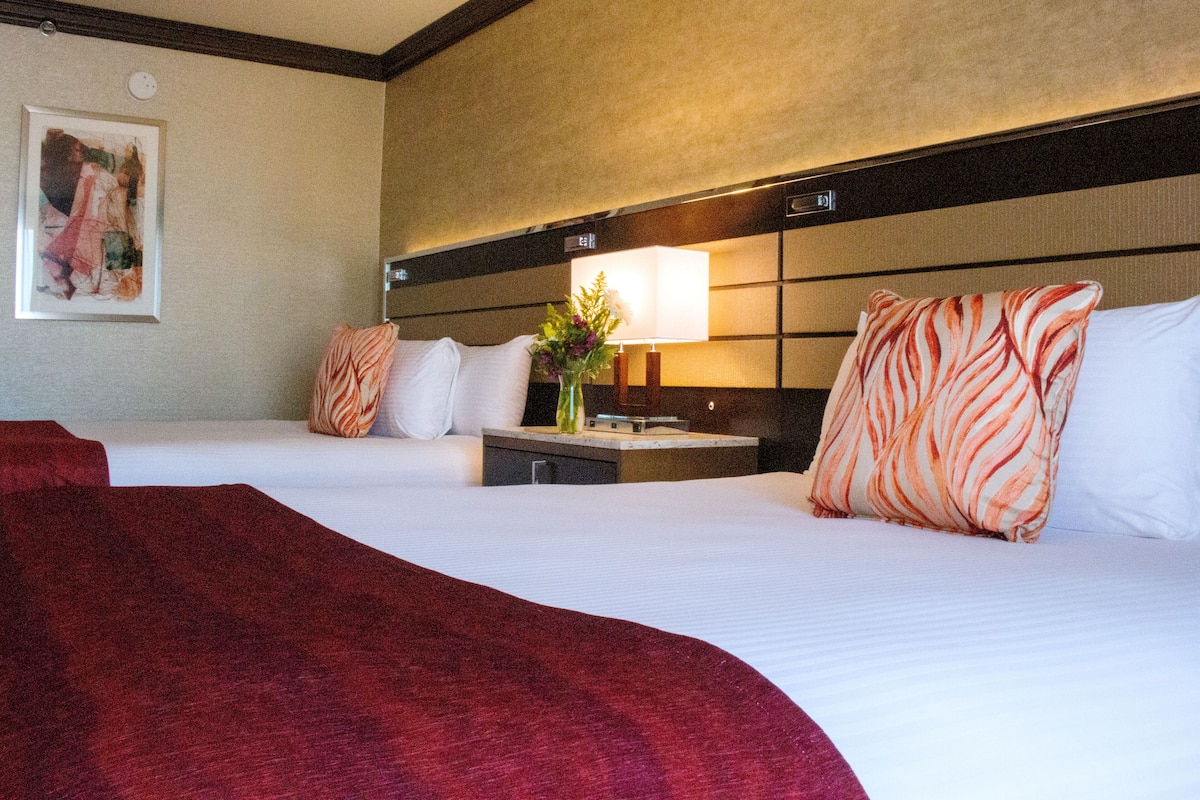 A hotel room with two beds, a nightstand, a lamp, and a painting on the wall.