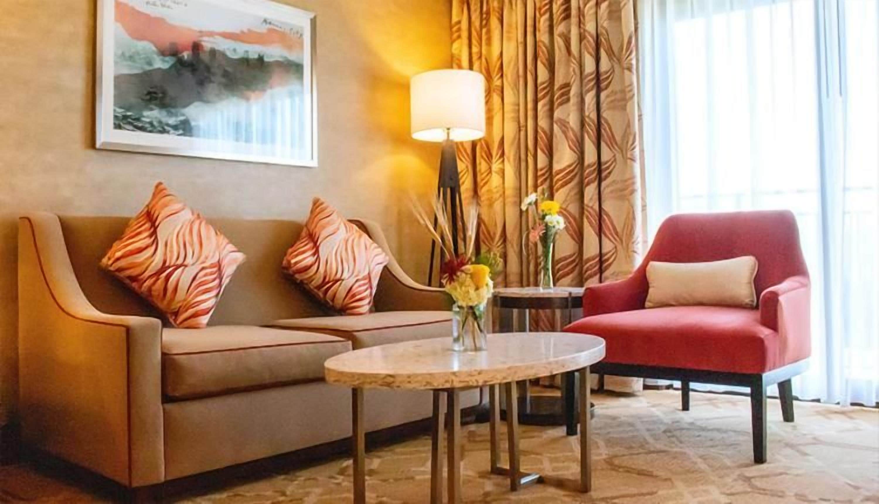 Et hotellobby med en sofa, en lænestol og et rundt bord med en vase med blomster.