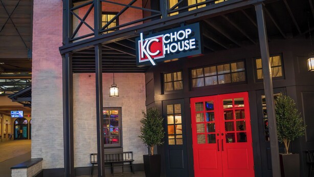 A building with a sign reading 'KC CHOP HOUSE,' a red door, and two potted plants.