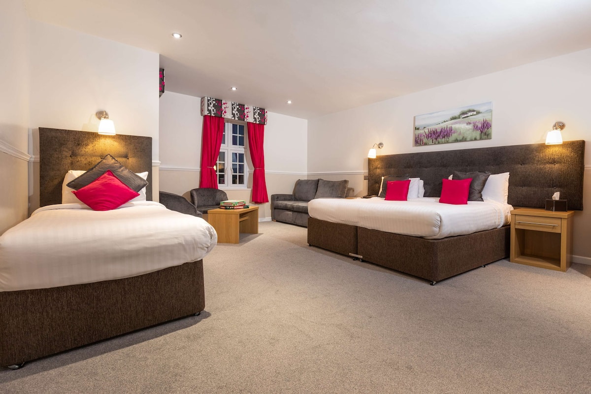 A hotel room with two beds, a sofa, a small table, and a chair.