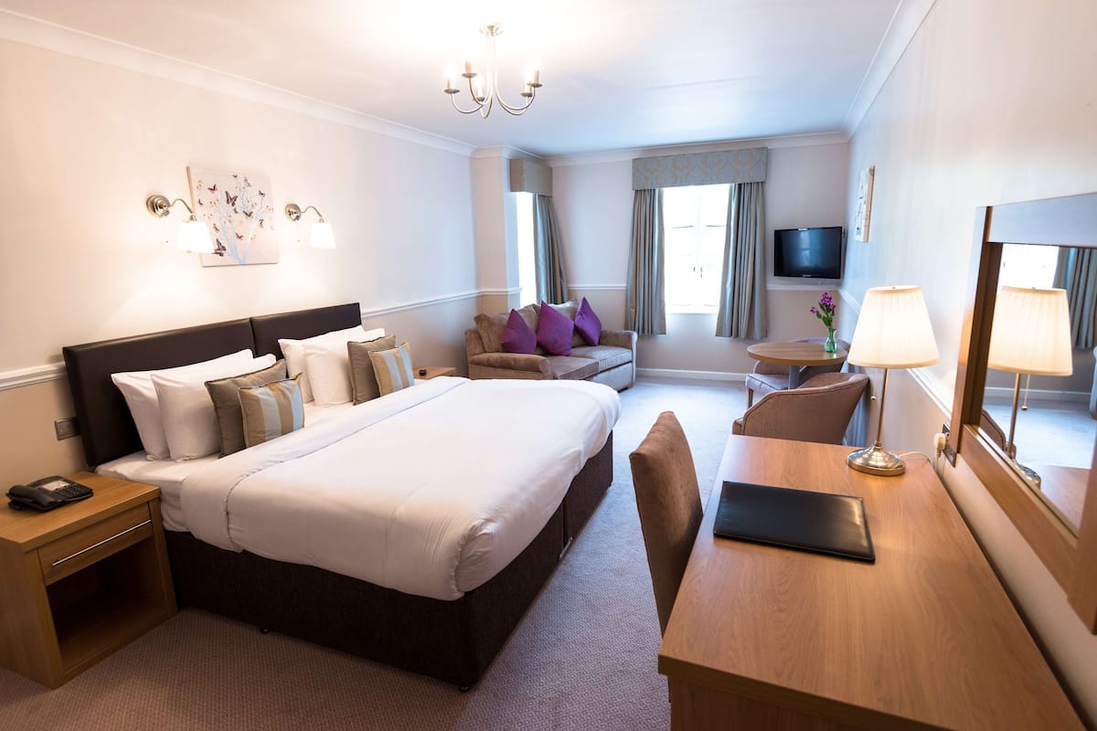 A hotel room with a large bed, bedside table, desk, chair, and a TV on the wall.