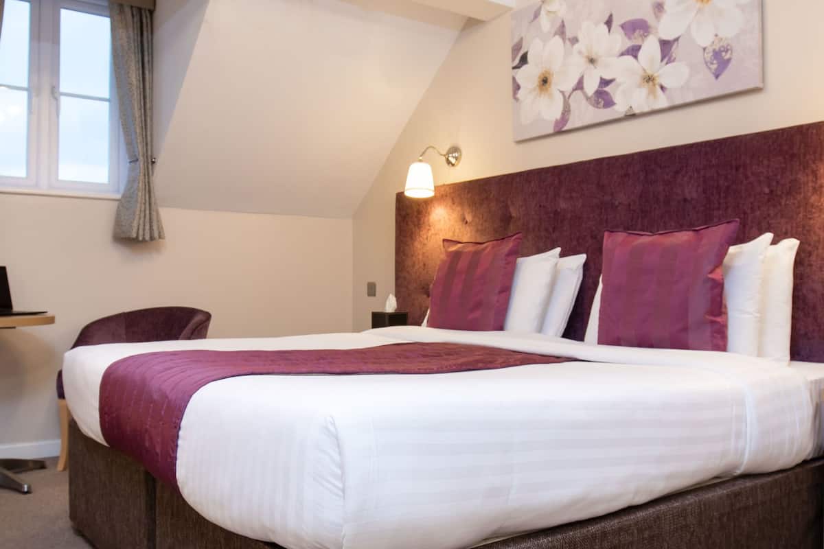 A hotel room with a bed, a desk, a chair, a small table, and a TV.