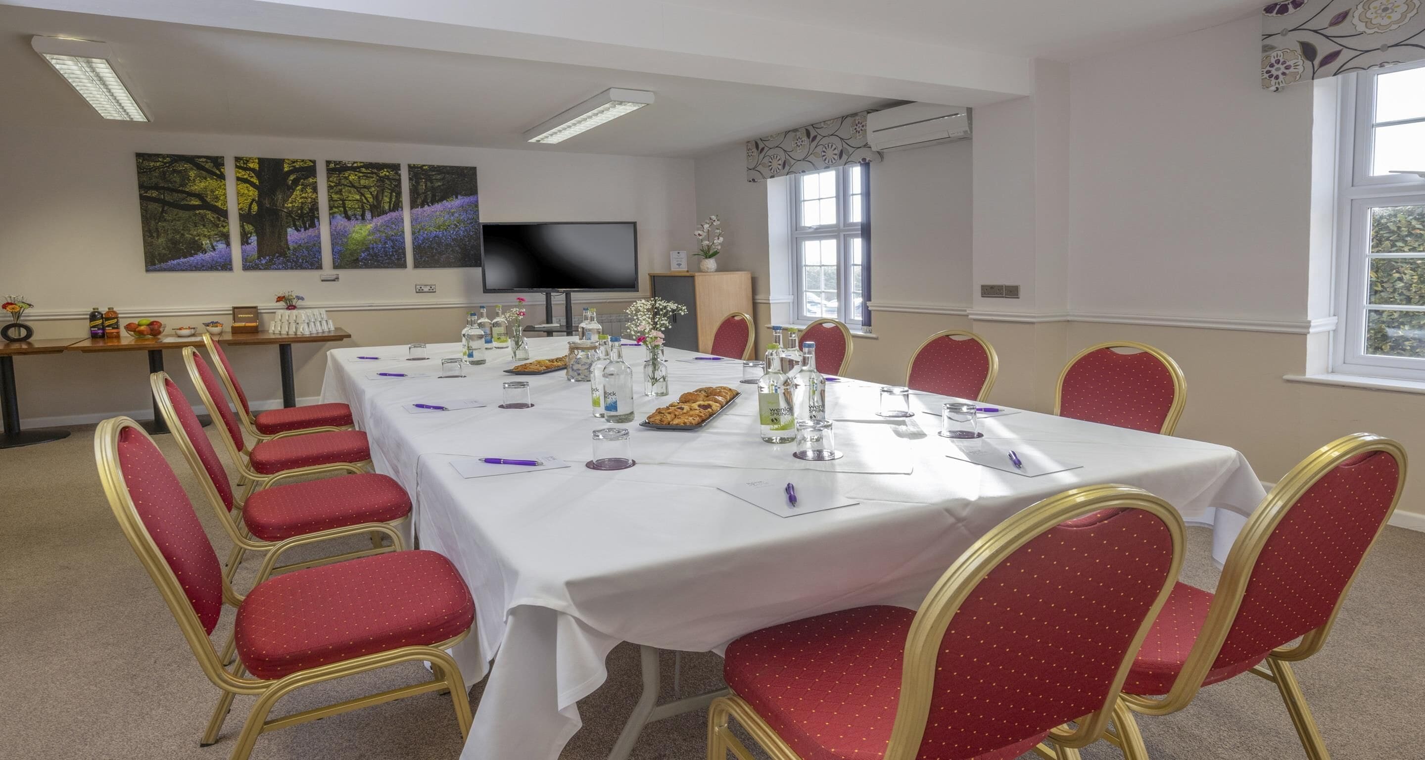 A conference room with a long table, red chairs, and a television on the wall.