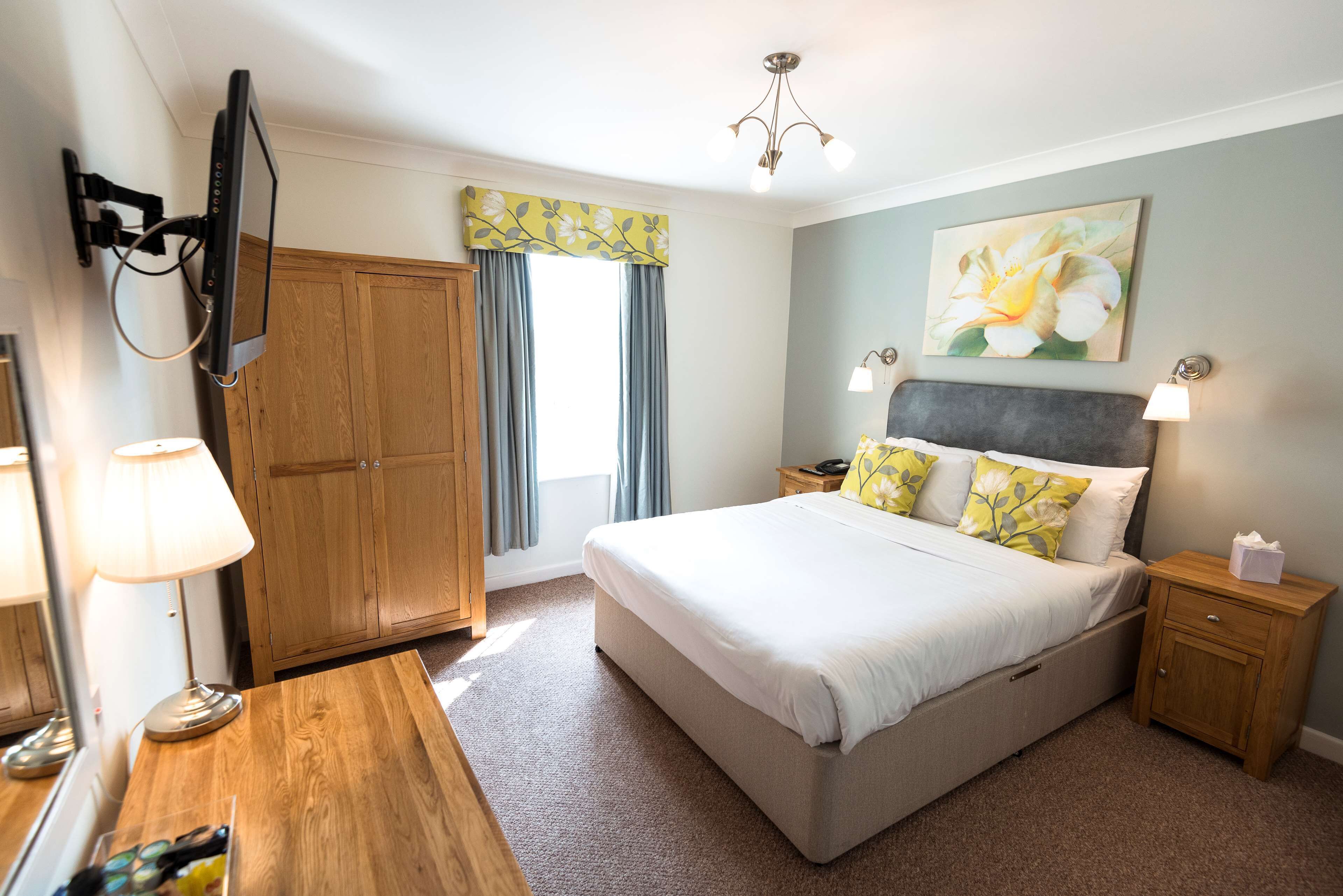 A bedroom with a bed, bedside tables, a TV mounted on the wall, a wardrobe, and a window with curtains.