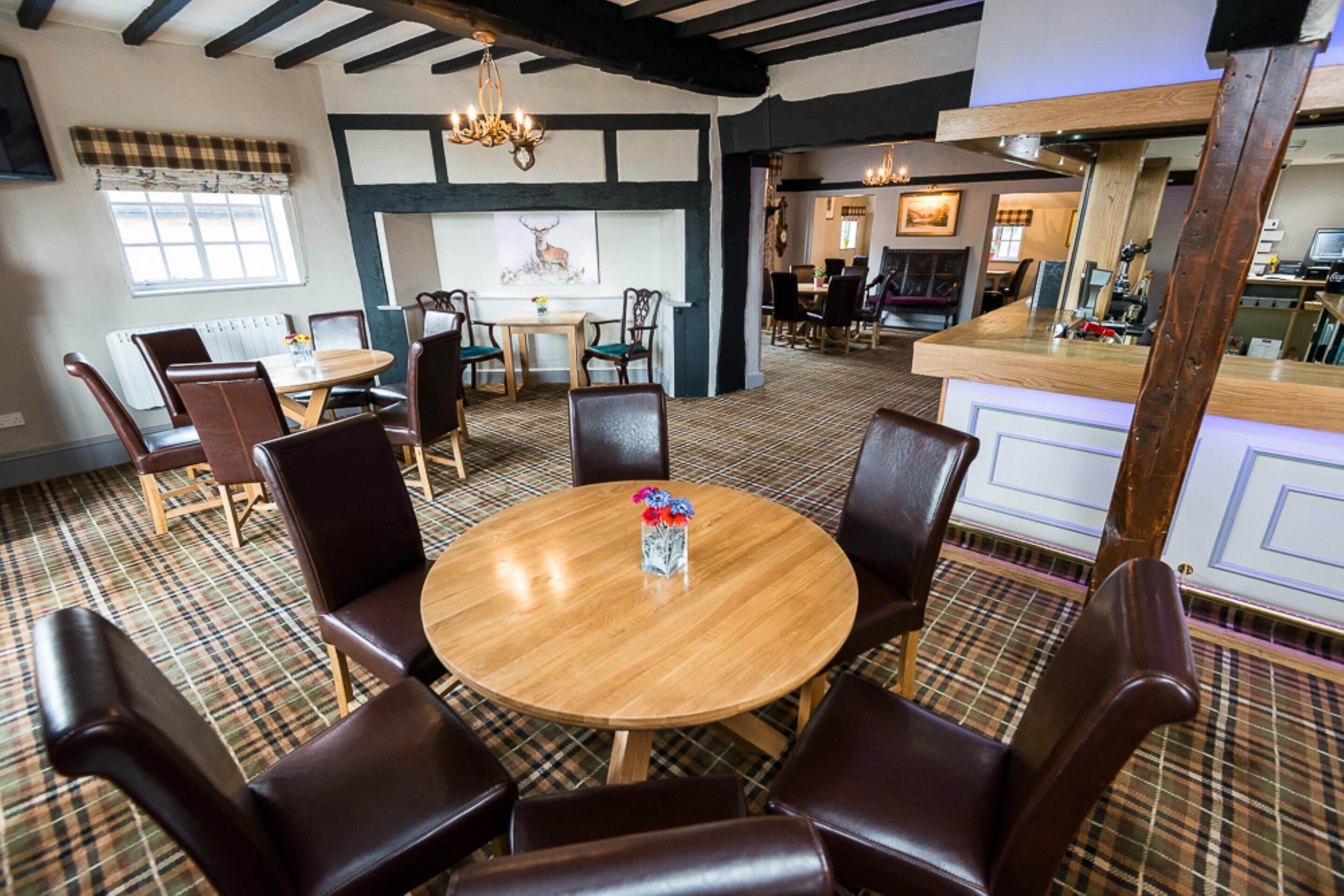 A dining area with a round wooden table surrounded by chairs, a chandelier, and a plaid-patterned floor.