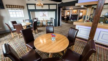 A dining area with a round wooden table surrounded by chairs, a chandelier, and a plaid-patterned floor.