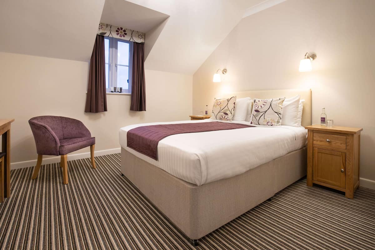 A bedroom with a large bed, a chair, a nightstand, and a window with curtains.