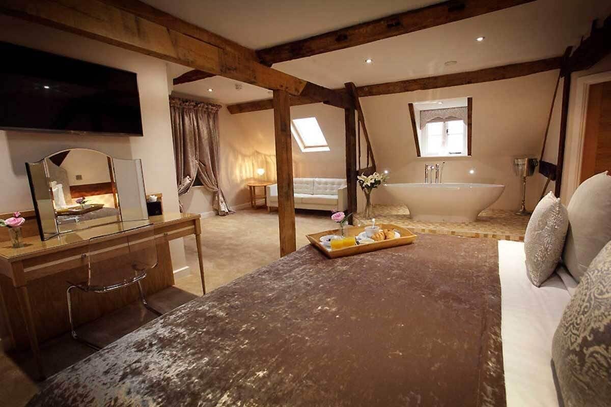 A bedroom with a wooden bed, a desk with a mirror, a television, a bathroom with a bathtub, and a skylight.