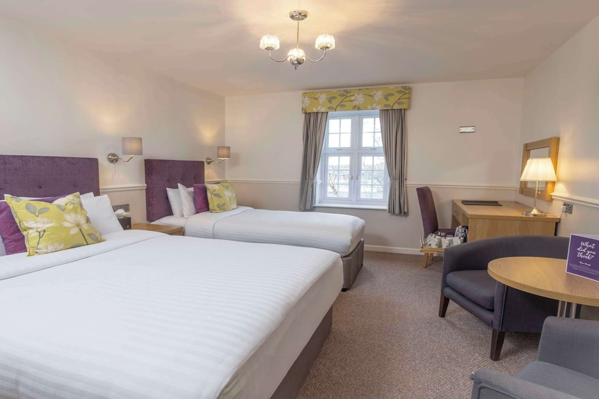 A hotel room with two beds, a desk, a chair, a lamp, and a window with curtains.