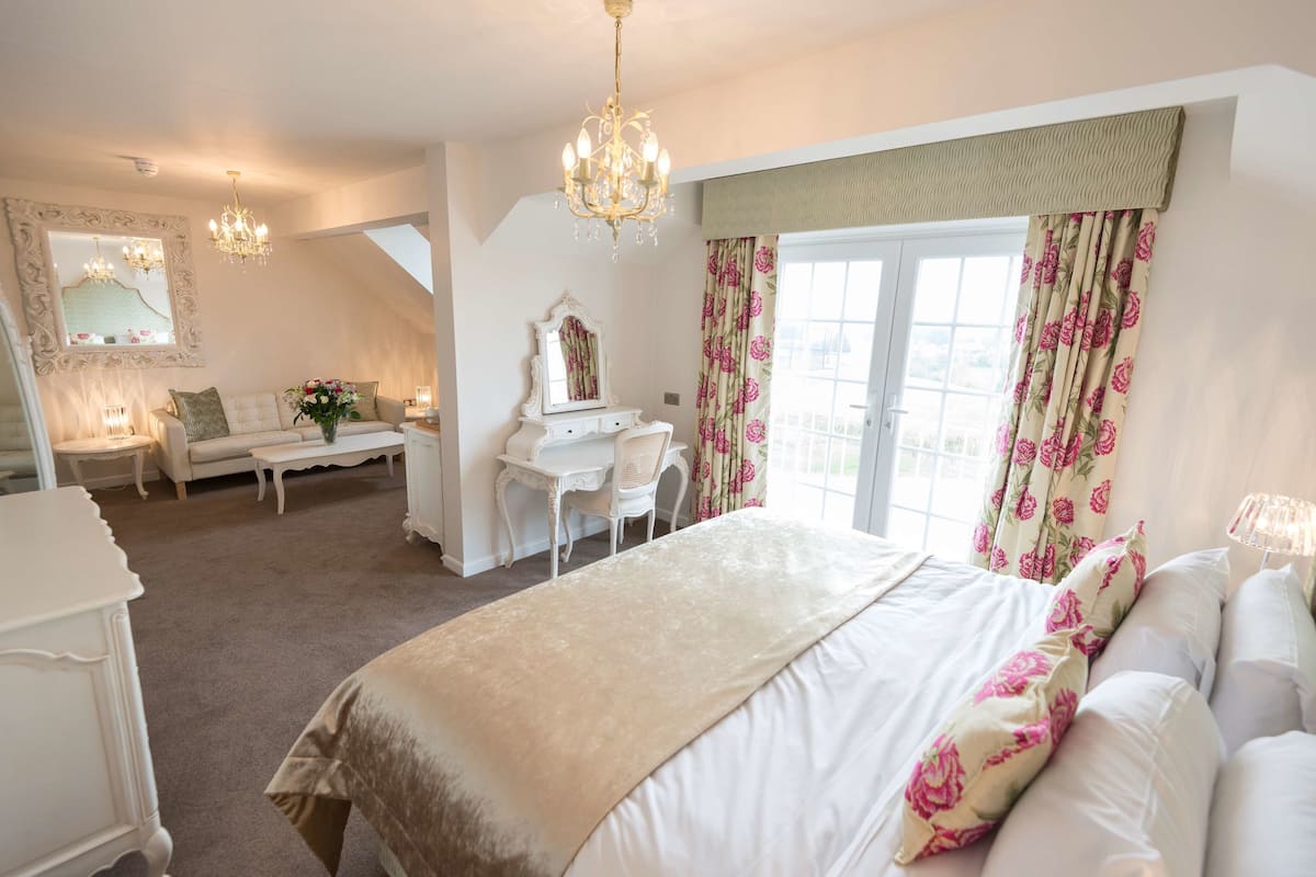 A bedroom with a large bed, a desk, a chair, and a mirror.