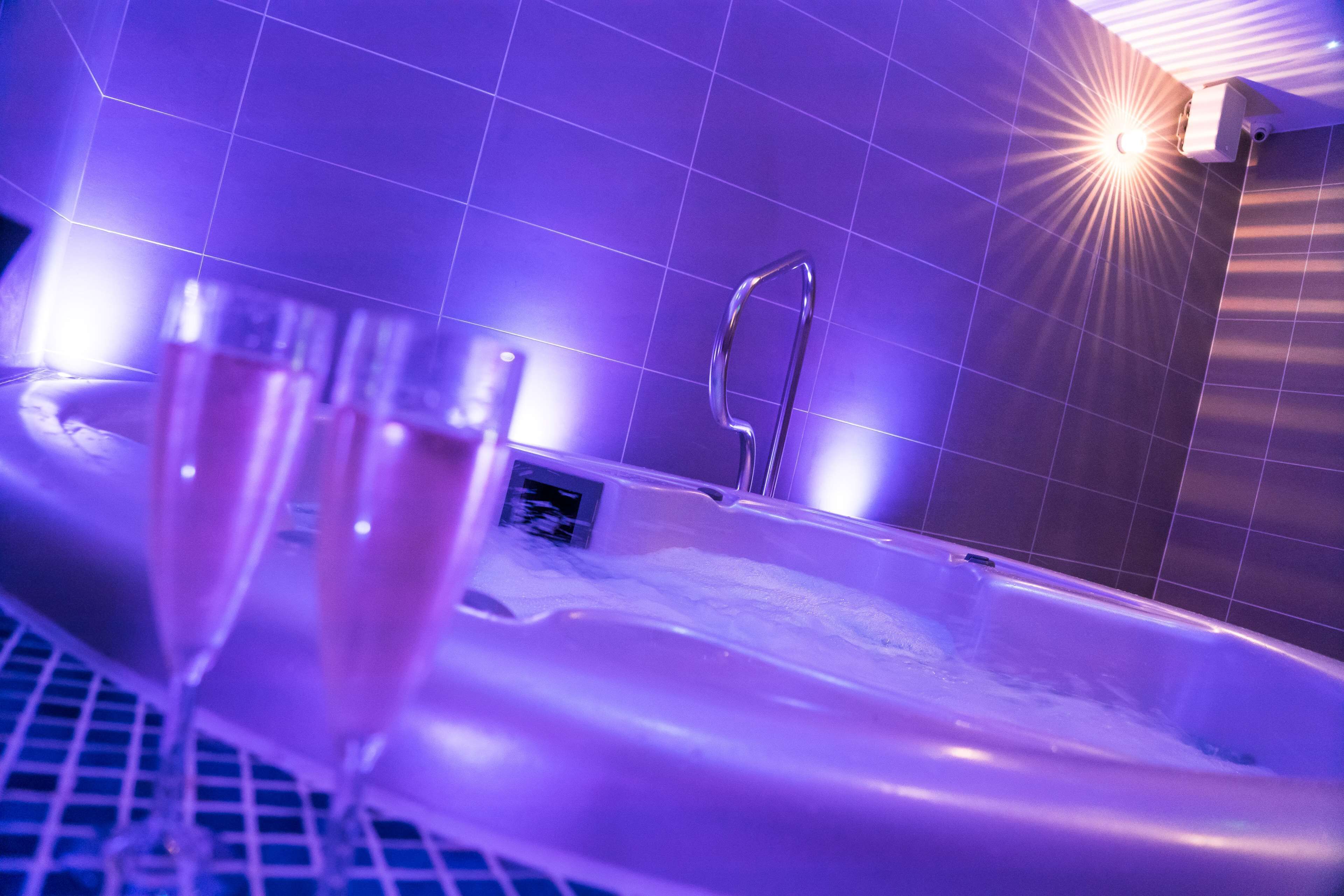 Una bañera de hidromasaje con baranda metálica, rodeada de baldosas de tono morado.