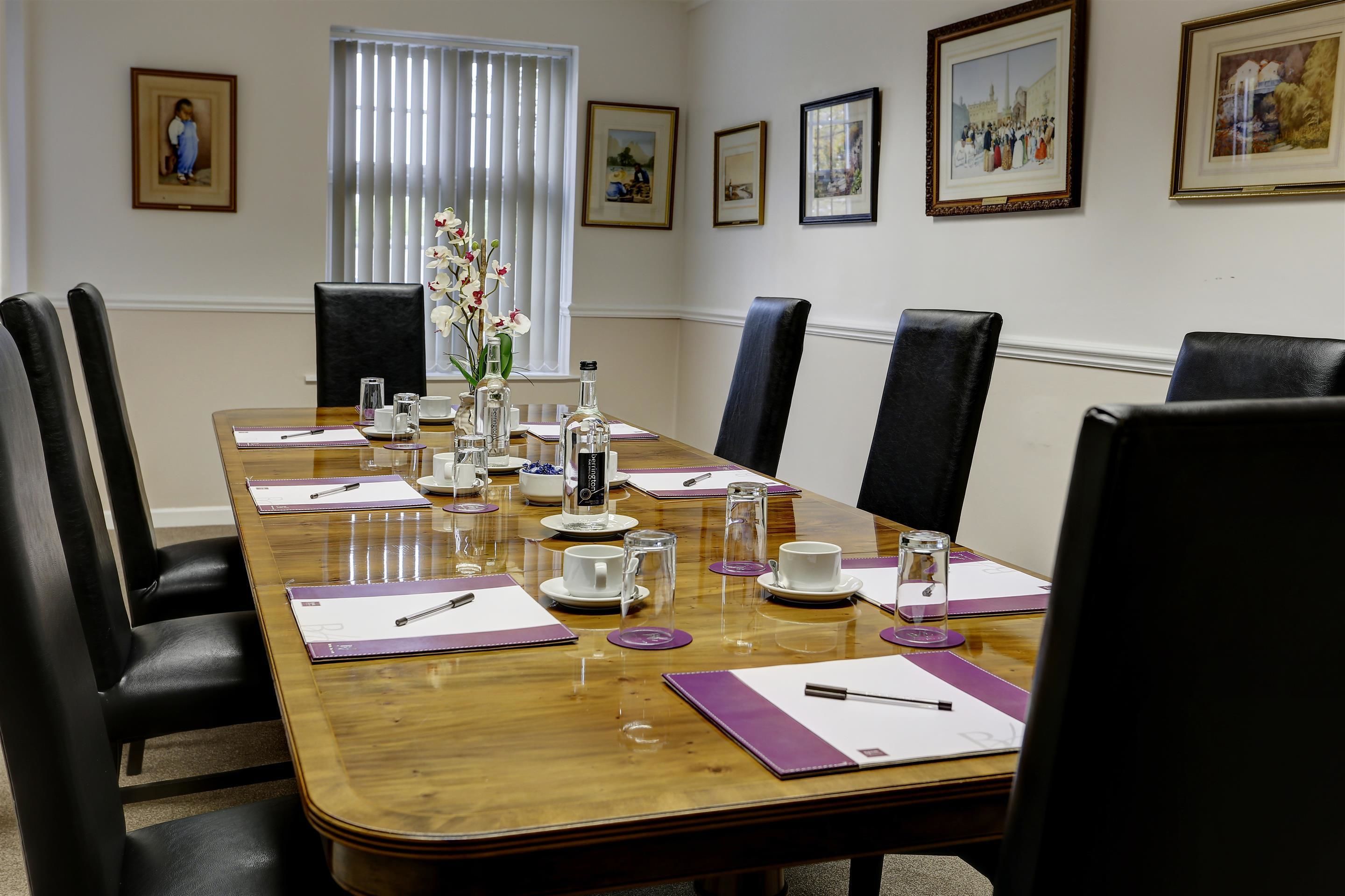 A conference room with a wooden table, black chairs, and framed pictures on the wall.
