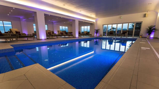 An indoor swimming pool with clear blue water, surrounded by lounge chairs and large windows offering views of the outdoors. - Worcester Bank House Hotel Spa & Golf, BW Premier Collection (Worcester)