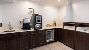 Eine moderne Küche mit dunklen Holzschränken, einer Edelstahlspüle, einer Kaffeemaschine, einem Getränkeautomaten und einem Kühlschrank.