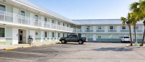 A motel with a parking lot, a single-story building with a flat roof, and a row of rooms with balconies.