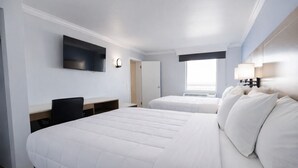 Ein Hotelzimmer mit zwei Betten, einem Schreibtisch, einem Fernseher und einem Fenster.