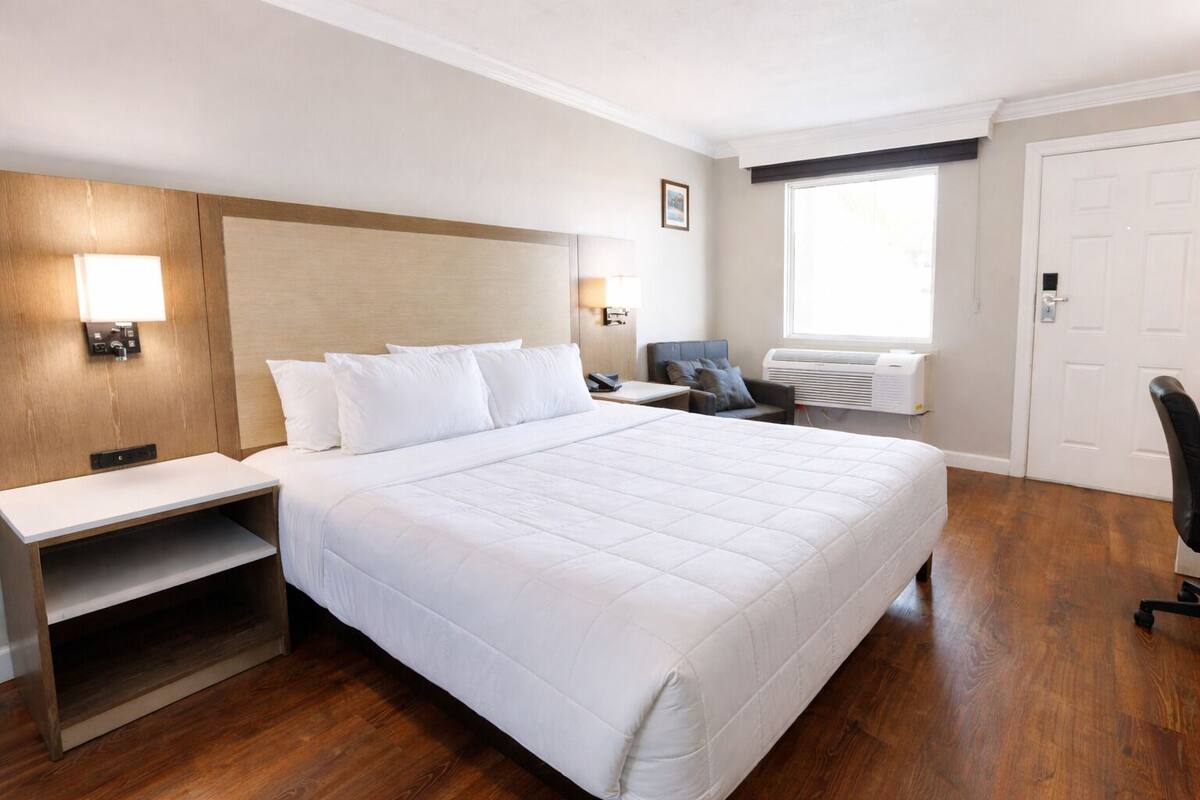 Une chambre d’hôtel avec un grand lit, un bureau, une chaise, une fenêtre et une porte.