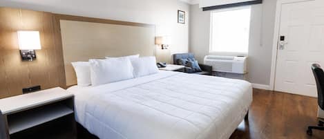 Une chambre d’hôtel avec un grand lit, des tables de chevet, un bureau, une chaise, un appareil de climatisation et une porte.